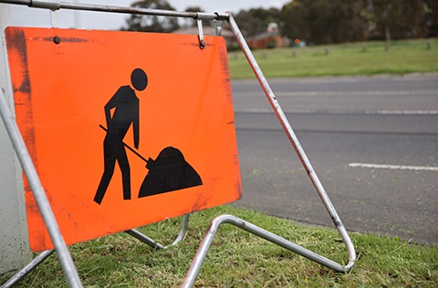 An orange road work warning sign placed on the grass beside an asphalt road.