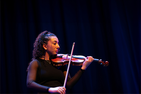 Violinist performing on stage under blue lighting, focused and mid-play.