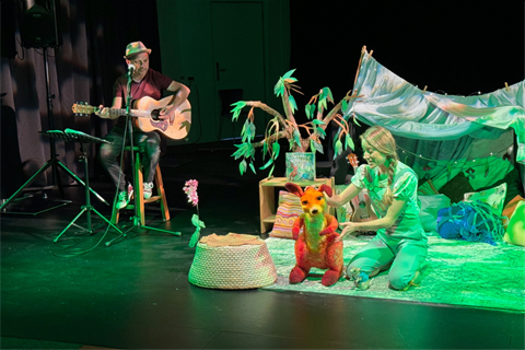 A musician plays a guitar. A young woman acts & interacts with a wallaby puppet.