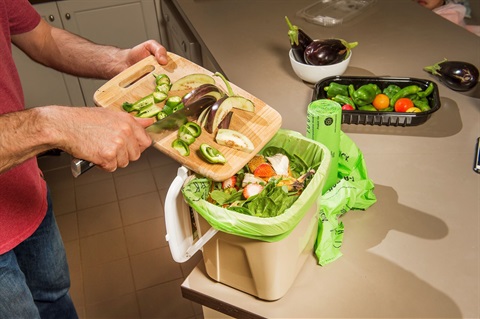 Close-up of food scraps being deposited into a kitchen countertop compost container.