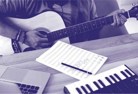 The workspace of a modern songwriter: guitar strings vibrating, notes being written.