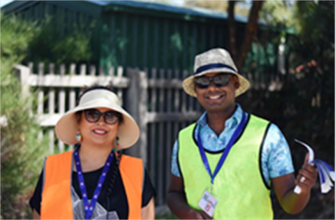Two volunteers in bright safety gear and hats during an outdoor event.