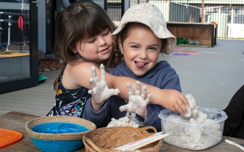 Two kindergarten kids happily playing with play dough at a play table.