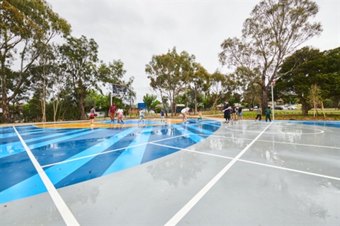 Young people playing basketball on a striped blue court
