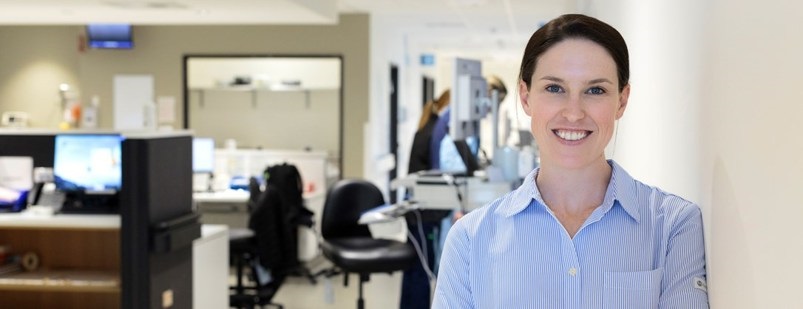 A person is in the foreground smiling. They are standing in a medical environment.