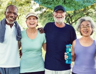 Four older people in leisure wear smile and laugh towards the camera.
