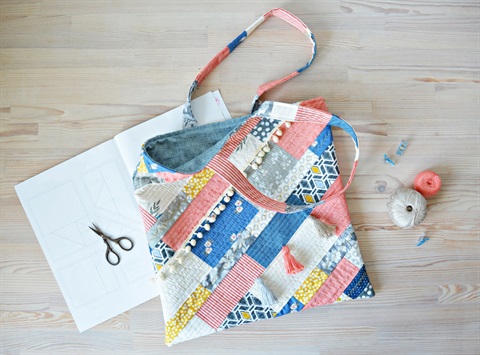 tote bag made from patchwork materials, with scissors, string, and paper arranged around the bag in a flatlay arrangement