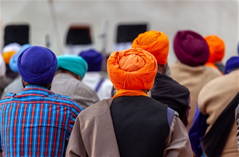 Sikh men in bright turbans stand close together at a gathering.