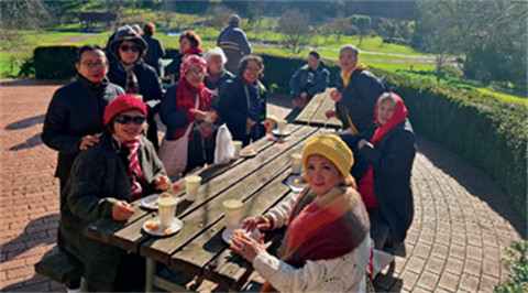 A vibrant group enjoys a scenic city bus tour, savoring refreshments amidst a picturesque garden setting.